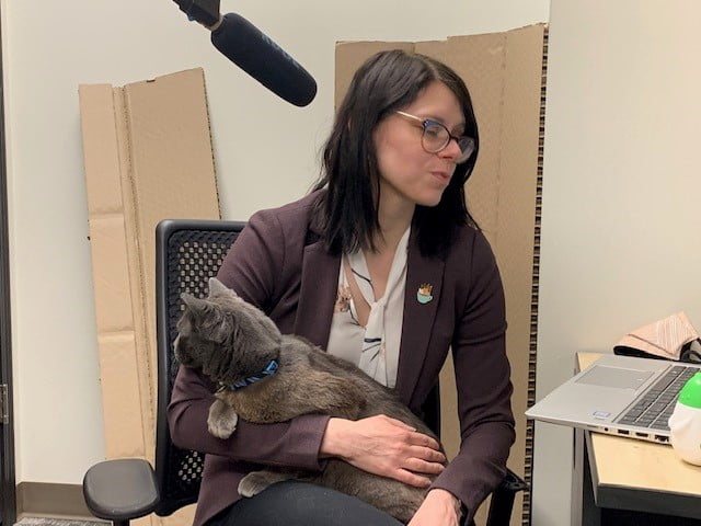 Director of Education , Melissa, holding her grey cat while speaking into a micros phone.